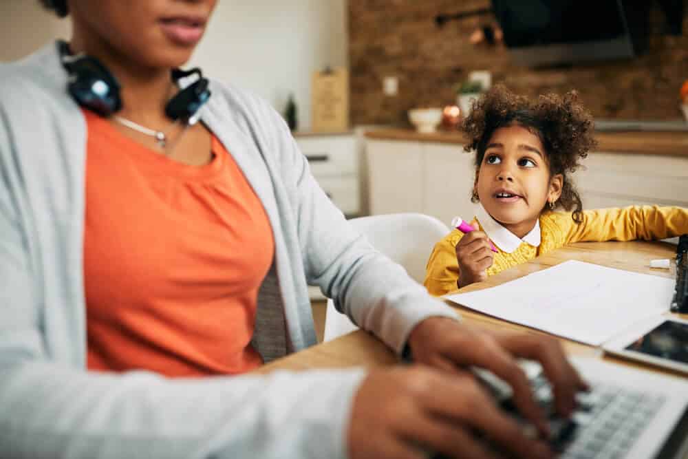 Busy mom working on side hustle while toddler sitting next to her.