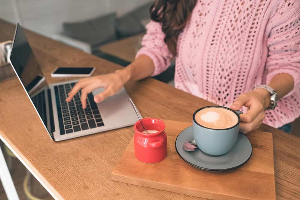 Mom in the morning with cup of coffee, blogging on laptop. Wearing pink sweater.