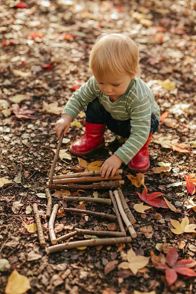 Child playing with sticks outdoors in autumn leaves.