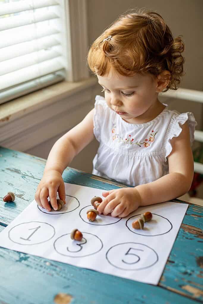 Colorful toddler activity with acorn caps and numbered circle worksheet.