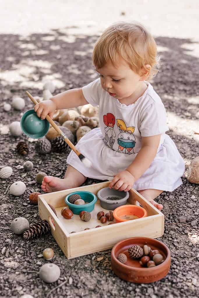 Small child playing with natural wood and silicone toy set outdoors.