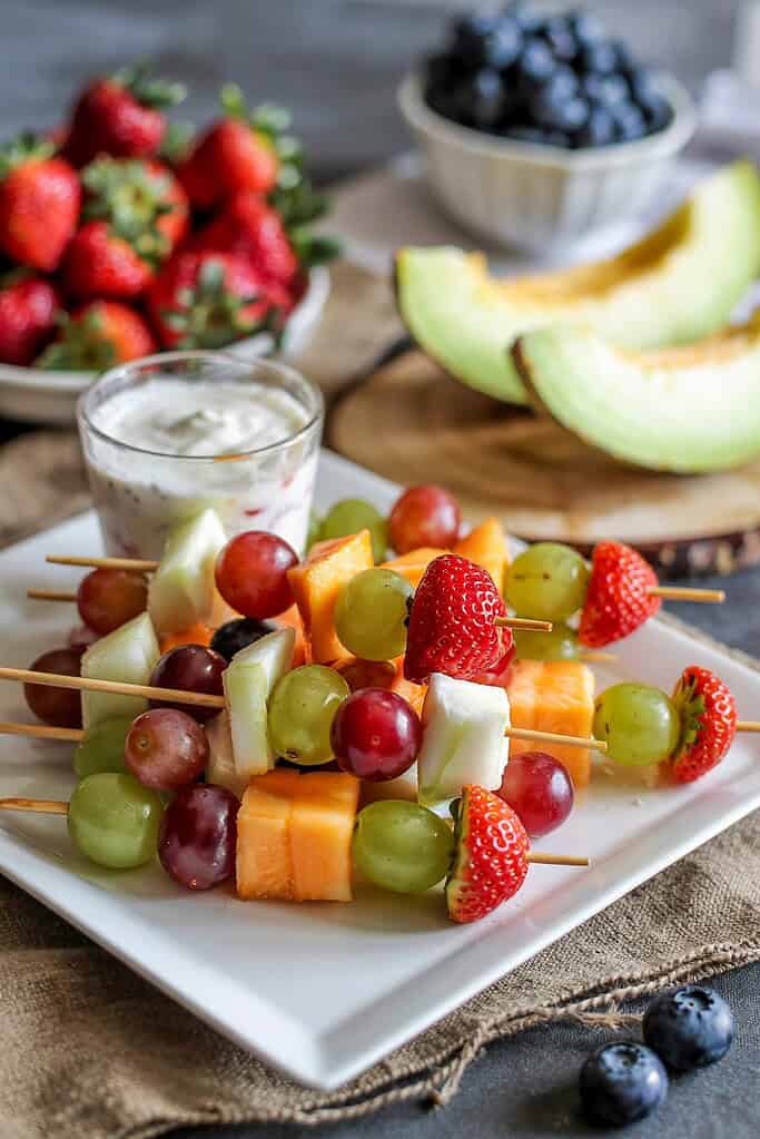 Colorful fruit kebabs with cubes of various fruits paired with a container of yogurt for dipping