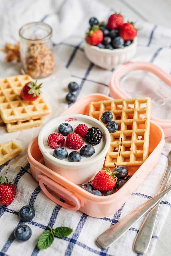 Mini whole grain waffles with yogurt dip and fresh berries packed for a breakfast-themed lunch.