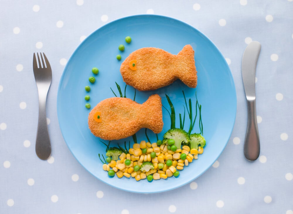 Blue plate of fish nuggets in the shape of little fish, with mixed vegetables.